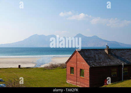 Un chalet en bois à la baie de Liag sur l'île de Eigg, avec le rhum dans la distance. Banque D'Images