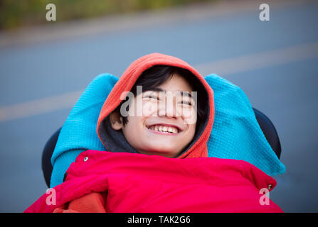 Smiling douze ans des besoins spéciaux à l'extérieur en fauteuil roulant enfant biracial sur la route par temps froid le port de pull et gilet Banque D'Images