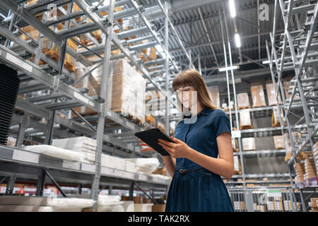 Entrepôt de gros. Belle jeune femme de magasin dans un centre commercial. Jeune fille à la recherche pour les produits d'une tablette est de vérifier les niveaux de stock dans un Banque D'Images