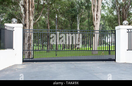 Metal entrée portes d'entrée de la propriété rurale mis en clôture en brique avec des lumières et de l'eucalyptus gum arbres en arrière-plan Banque D'Images