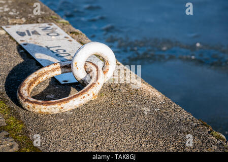 Close up d'un anneau d'amarrage en métal rouillé partiellement sur un quai le long d'un canal Banque D'Images