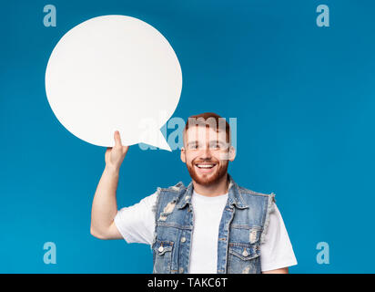 Smiling young man holding blank speech bubble et looking at camera Banque D'Images