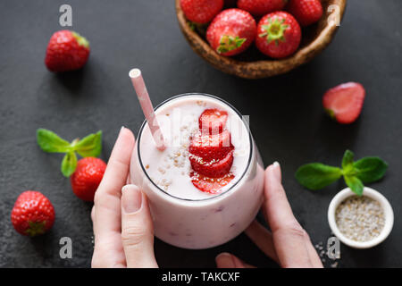 Smoothie aux fraises milkshake ou en verre sur fond noir. Mains tenant rempli de boisson d'été. Concept de saine alimentation Banque D'Images