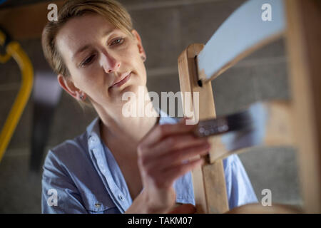 Femme mature à l'atelier de meubles Upcycling Accueil Peinture chaise en bois Banque D'Images