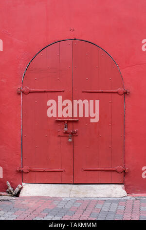 Style ancien porte en bois haut voûté peint en rouge foncé situé dans la paroi rouge. Banque D'Images