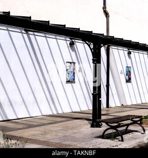 Auvent en bois noir jette une ombre sur un mur peint en blanc couvrant un trottoir et banc en bois. Banque D'Images