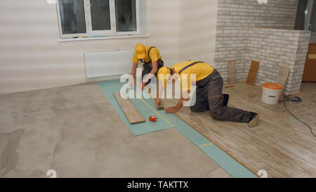 Pose des travailleurs de parquet stratifié. Les constructeurs professionnels travaillent à l'étage dans maison neuve. Concept de rénovation. Banque D'Images