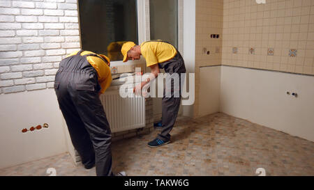 Les travailleurs professionnels l'installation de chauffage dans la nouvelle chambre. Comment remplacer un radiateur. Service de réparation. Banque D'Images