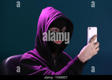 Femme hacker en masque et avec un téléphone mobile sur un fond de couleur Banque D'Images