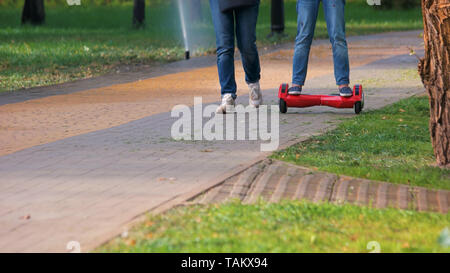 Les jambes des filles sur hover board en parc d'été. Les gens la marche à l'extérieur. Loisirs et vie active. Banque D'Images