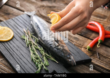 Woman squeezing jus de citron sur le maquereau, poisson savoureux closeup Banque D'Images