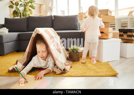 Les enfants s'installer à nouveau vacances : petit garçon couché au plaid sur tapis et dessin photo tandis que sa jeune sœur déballage Banque D'Images