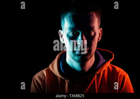 Un adulte guy s'hâte dans une orange Sweat capuche en bleu et rose sur les côtés avec un sourire sur un fond noir isolé. Banque D'Images