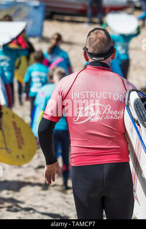 Un instructeur de surf avec l'École de Surf de la plage de Fistral de partir à exécuter une leçon de surf à Newquay en Cornouailles. Banque D'Images