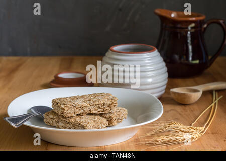 Les barres de céréales de blé sec en assiette petit-déjeuner sur la table en bois avec les épis de blé en premier plan et le miel et le lait pot en arrière-plan Banque D'Images