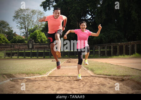 Deux sports partenaires sont le jogging ensemble sur une journée ensoleillée portant des chemises orange et rose. Ils se regardent et sourire, profiter les sports qu'ils ne Banque D'Images