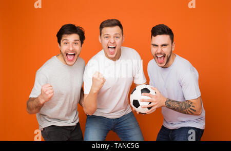 Des fans de football. Les hommes Holding Soccer Ball, fond orange Banque D'Images