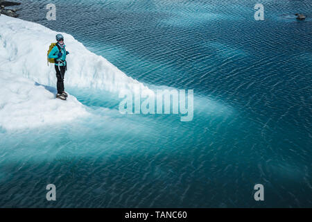 Une femme debout avec un casque et un pack près du bord d'un lac bleu. Le lac est sur le dessus de la Matanuska glacier des montagnes Chugach, de l'EC Banque D'Images