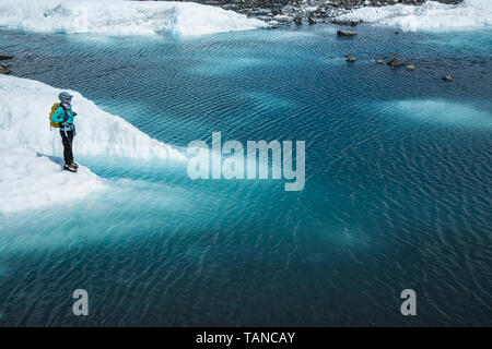 Guide d'une femme debout près du bord d'un profond lac supraglaciaire sur la Matanuska Glacier en Alaska. Banque D'Images
