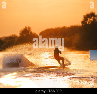 La planche de surf un Ollie saut à coucher du soleil doré. Wakeboarder qualifiés faisant Ollie sauter, projections d'eau tombe dans l'appareil photo. Jeune homme équitation c Banque D'Images