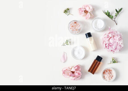 Beauté style de composition. Pot de crème de peau, tonicum bouteille, roses, pivoine fleur et sel de l'himalaya sur arrière-plan du tableau blanc. Cosmétiques Bio, spa Banque D'Images