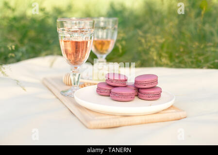 Rose clair et rose fushia macarons macarons français ou en verre avec des gobelets de vin rose à une plaque blanche sur une nappe beige background Banque D'Images