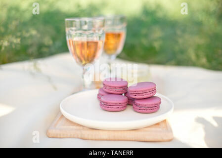 Rose clair et rose fushia macarons macarons français ou en verre avec des gobelets de vin rose à une plaque blanche sur une nappe beige background Banque D'Images