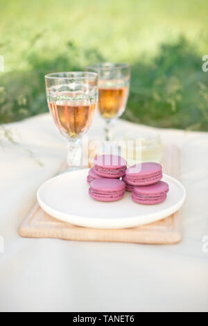 Rose clair et rose fushia macarons macarons français ou en verre avec des gobelets de vin rose à une plaque blanche sur une nappe beige background Banque D'Images