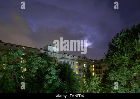 Les bâtiments et les arbres verts dans la nuit, illuminé le ciel pendant un orage Banque D'Images
