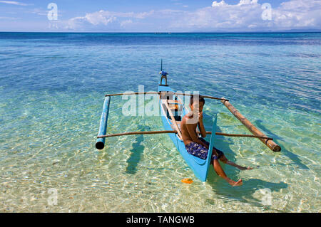 Filipino garçon assis sur un petit bateau outrigger à Bounty beach, Malapascua Island, Cebu, Philippines Banque D'Images