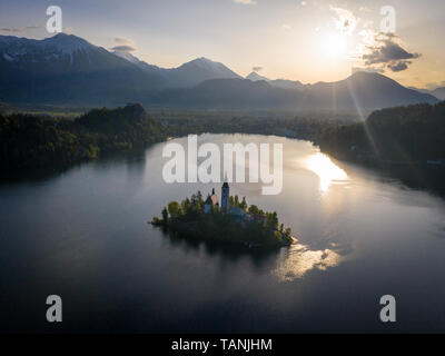 Le lac de Bled Vue aérienne de l'église peu de temps après le lever du soleil. Tour de l'église Sainte-Marie de l'Assomption : église dans l'ombre. Il y a des Alpes Juliennes en backgrou Banque D'Images