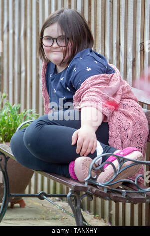 Fille avec le syndrome de Down assis sur un banc de jardin profiter de la vie et le jardin. Banque D'Images