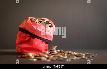 Pièces de métal dans un sac rouge s'est étendu à la table. Fond sombre. L'argent d'épargne ou concept. Banque D'Images