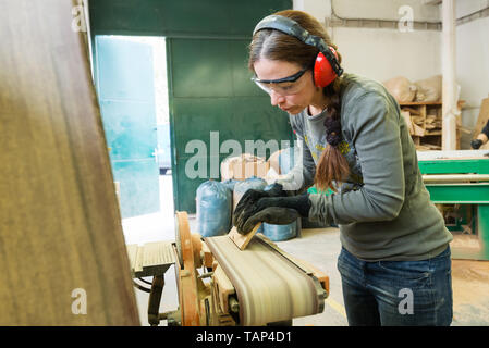 Jeune femme à l'aide d'une ponceuse de ceinture de sable de planche en bois à l'atelier Banque D'Images