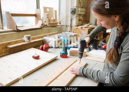 Jeune femme à l'aide de tournevis électrique sur un morceau de bois à l'atelier Banque D'Images