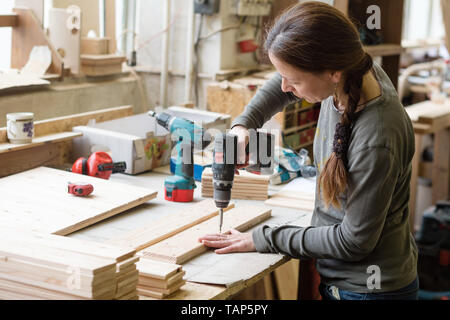 Jeune femme à l'aide d'un tournevis électrique sur un morceau de bois à l'atelier Banque D'Images