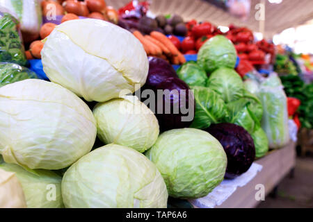 Gros plan du blanc, rouge et le chou vert empilés sur le comptoir du marché dans le contexte de troubles d'autres légumes à la lumière du jour. Banque D'Images