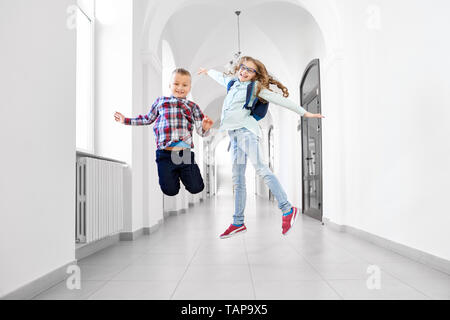 Heureux, joyeux écoliers s'amuser après les cours de l'école dans le couloir. Jolie fille positive, avec sac à dos pour l'école et beau garçon souriant et le saut. Banque D'Images