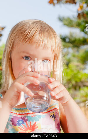 Petite fille blonde de boire l'eau du robinet fraîche et pure dans un verre dans un jardin d'été - concept de vie sain Banque D'Images