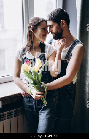 Couple heureux se tient près de la fenêtre avec des tulipes et de se toucher Banque D'Images