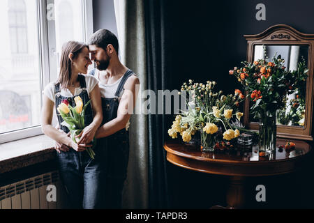 Couple heureux s'embrassent près de la fenêtre et une table avec des roses et des tulipes Banque D'Images