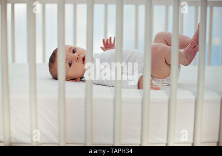 Portrait d'un petit garçon agitant ses jambes en l'air alors qu'il se trouve son berceau. Banque D'Images