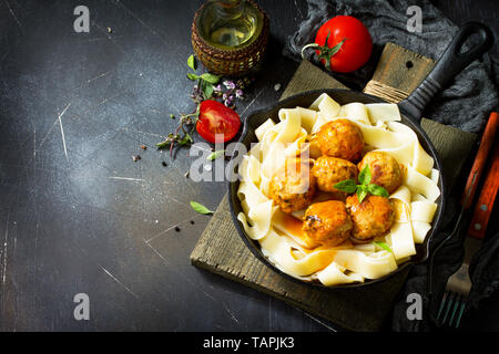 Pâtes pâtes fraîches et des boulettes de boeuf à la sauce tomate dans une poêle à pierre sombre tableau. Espace libre pour votre texte. Banque D'Images