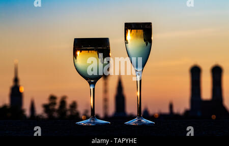 26 mai 2019, Bavaria, Munich : au coucher du soleil, deux verres de vin blanc debout sur le mur de l'allée du parlement bavarois en face de la skyline de la capitale bavaroise. Dans l'arrière-plan vous pouvez voir les tours de la vieille pierre', l'hôtel de ville (M) et l'église Frauenkirche (r). Photo : Peter Kneffel/dpa Banque D'Images