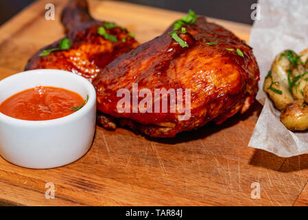 Cuisses de poulet fumé servi avec des pommes de terre et la sauce sur plateau en bois fermer Banque D'Images