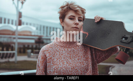 Portrait de jeune femme tenant sa planche à roulettes. Femme avec du patinage à skate park à la recherche à l'extérieur de l'appareil photo Banque D'Images