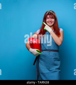 Photo de femme avec fleuriste arrosoir en mains de doigt à l'autre sur fond bleu vide. Banque D'Images