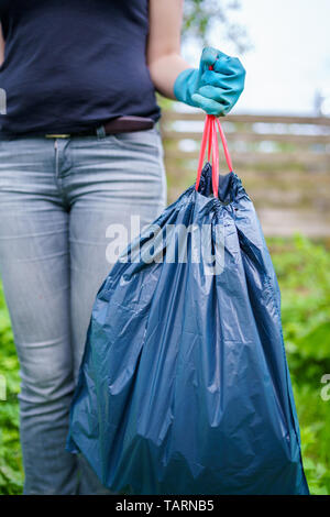 Image de la femme dans les gants en caoutchouc avec un sac poubelle sur le jardin en été Banque D'Images