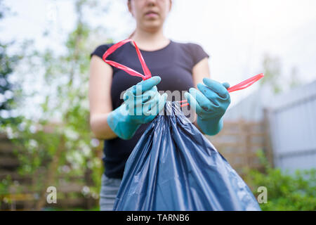 Image de la femme dans les gants en caoutchouc avec un sac poubelle sur le jardin en été Banque D'Images