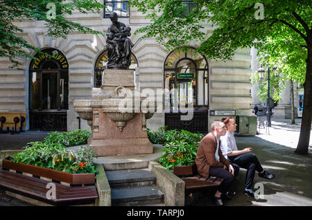 Un couple s'asseoir sur un banc en face de l'ex-maternité de la fontaine d'eau potable sur l'avenue Royal Exchange à Londres, Royaume-Uni Banque D'Images